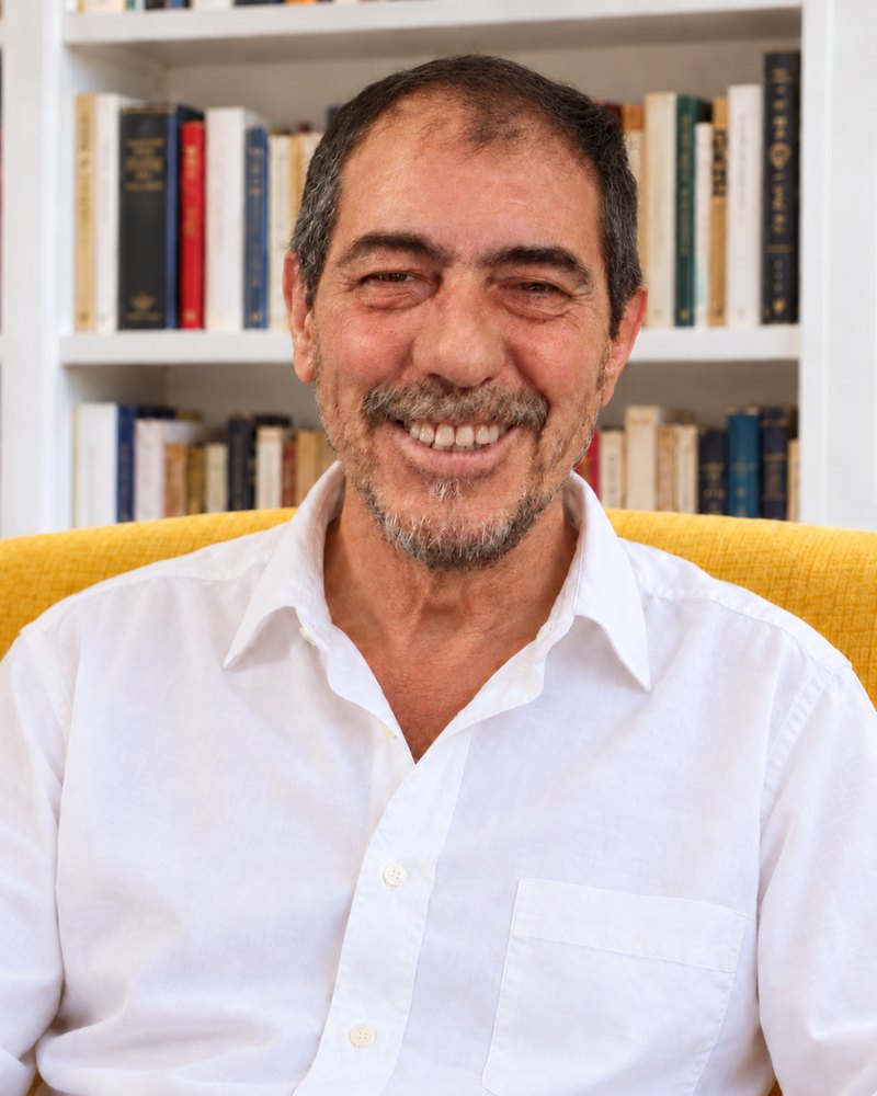 Roberto González de Cuenca, sonriente, con camisa blanca, sentado en un sillón amarillo ante una librería